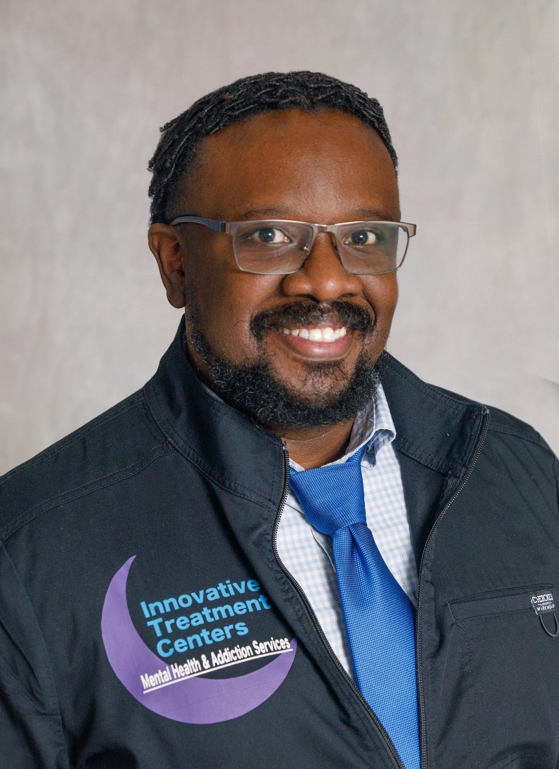 Smiling professional in glasses and tie, wearing an Innovative Treatment Centers pin and jacket