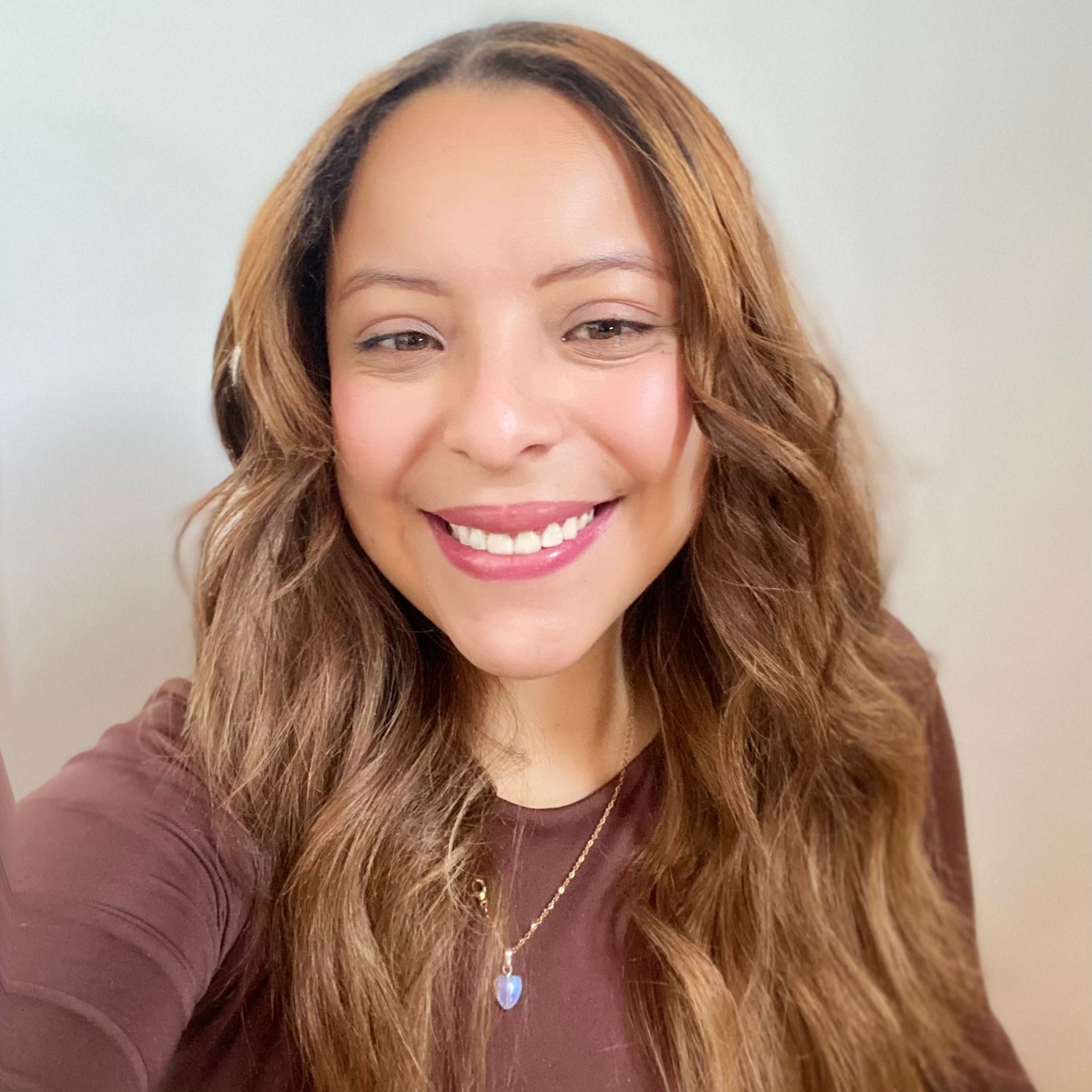 Smiling woman with long wavy brown hair in a mauve top against a light background