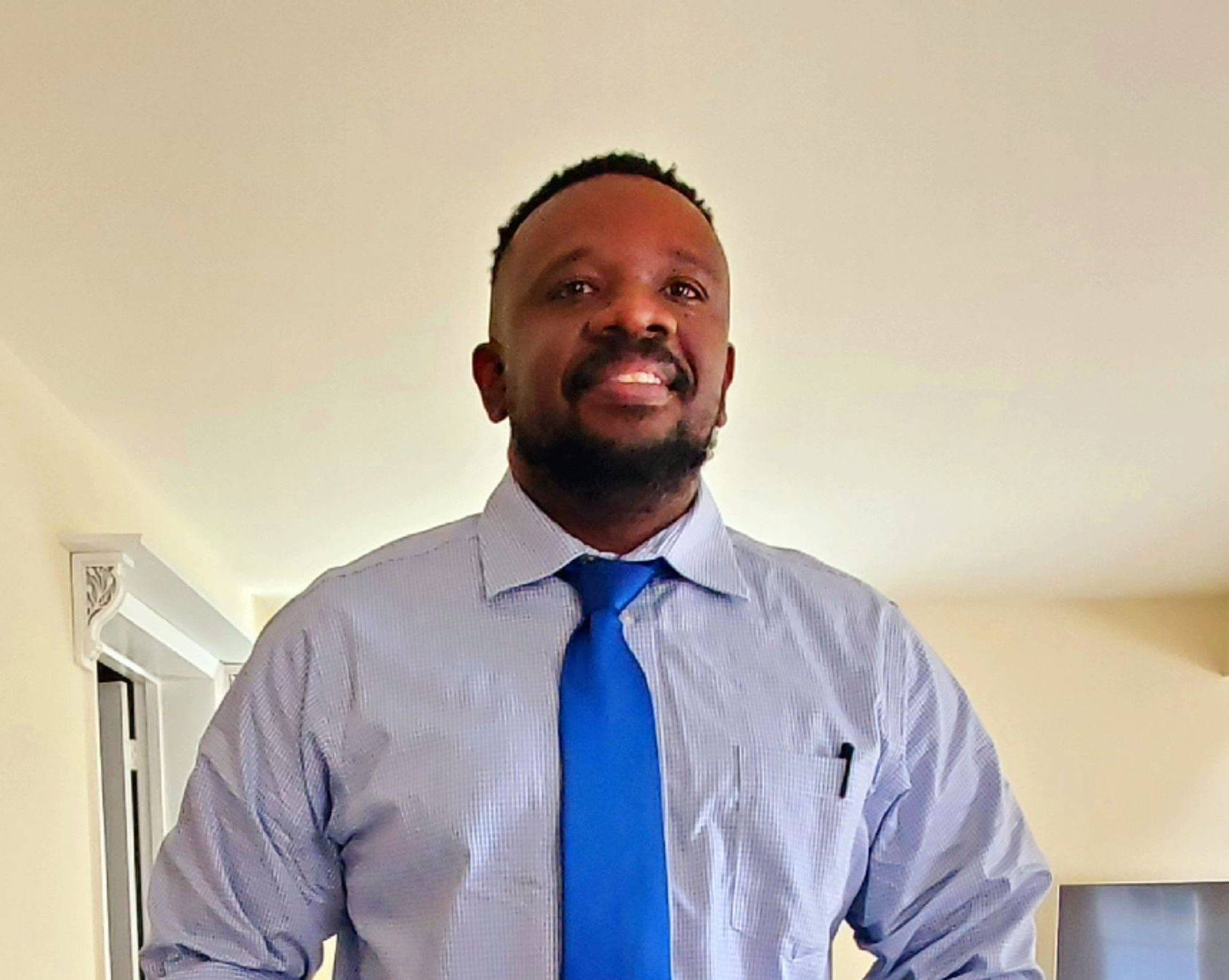 Smiling person in a blue tie and striped shirt standing indoors