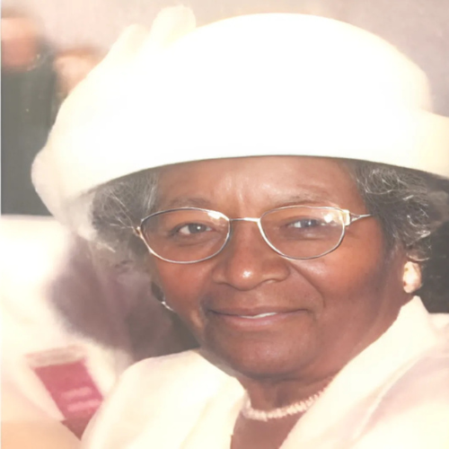 A woman wearing glasses and a white hat is smiling for the camera