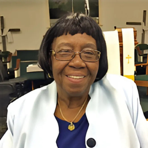 A woman wearing glasses and a blue shirt is smiling in a church