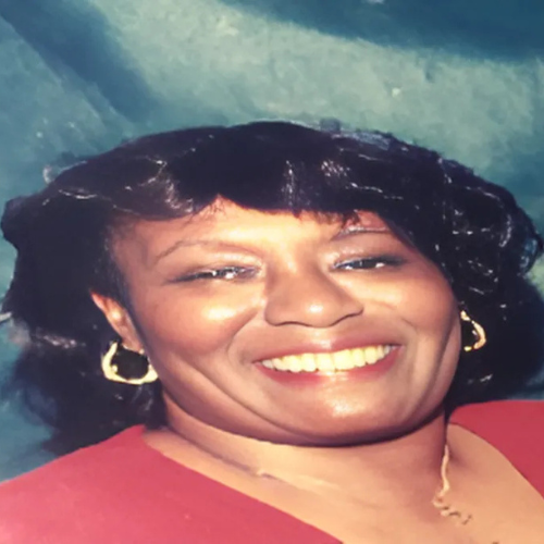 A woman wearing a red shirt and gold earrings smiles for the camera
