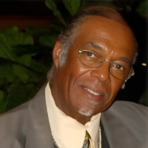 A man wearing glasses and a suit smiles for the camera