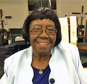 A woman wearing glasses and a blue shirt is smiling in a church.