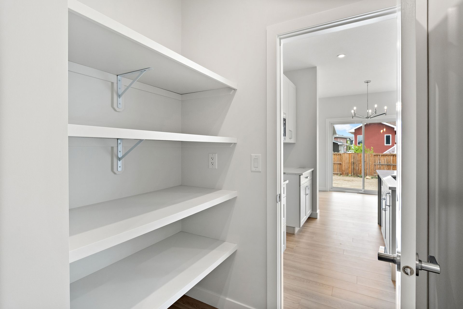 Bright walk-in closet with white shelves opening to a light hallway and kitchen beyond