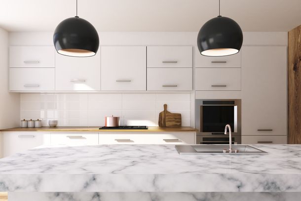 Modern white kitchen with marble island, black pendant lights, and built-in oven