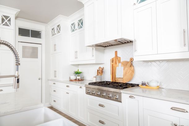 Bright white kitchen with cabinets, gas range, marble counters, and a farmhouse sink