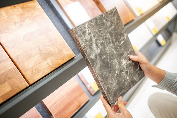 Person holding a dark marble tile while browsing wood and stone samples on a showroom display.