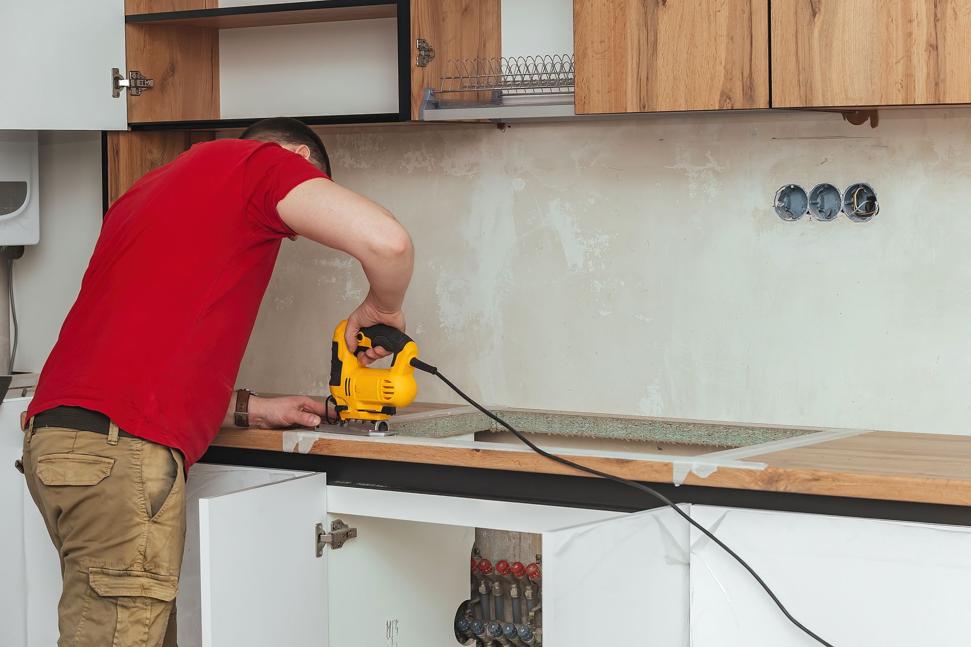 Person using a yellow power tool to cut a countertop in a kitchen under renovation