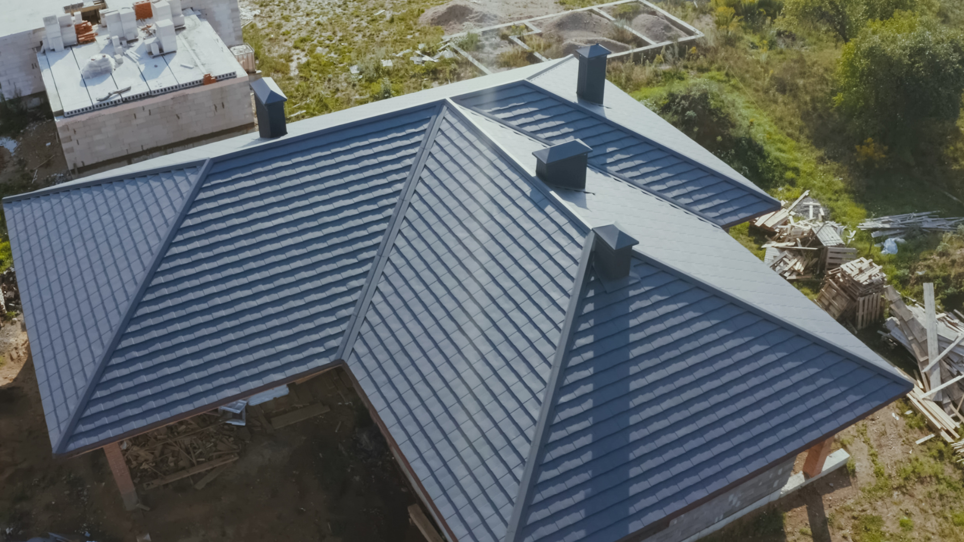 Dark metal roof on a building with three chimneys, aerial view.