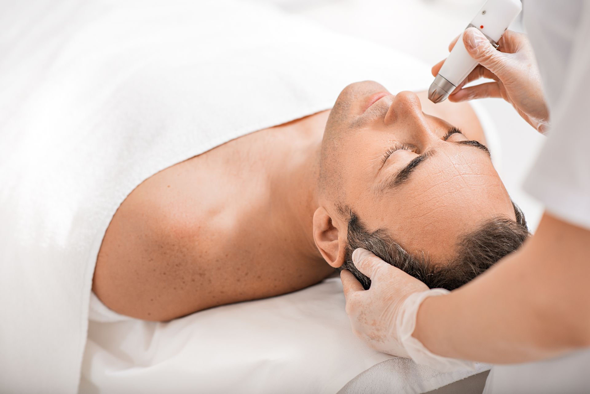 Person receiving facial skin treatment with a handheld device; gloved hands, close-up.