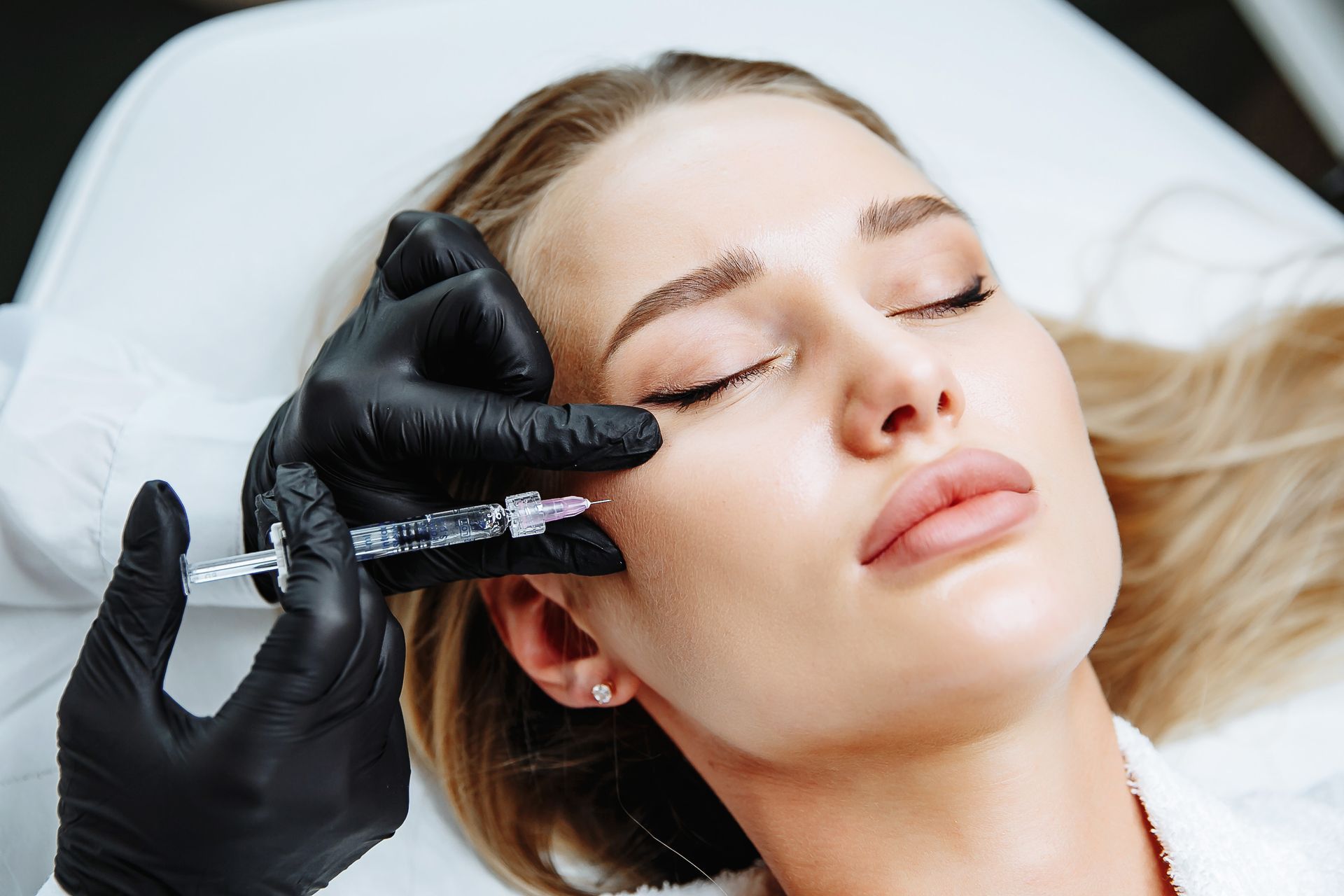 Person receiving facial injection, hands wearing black gloves.