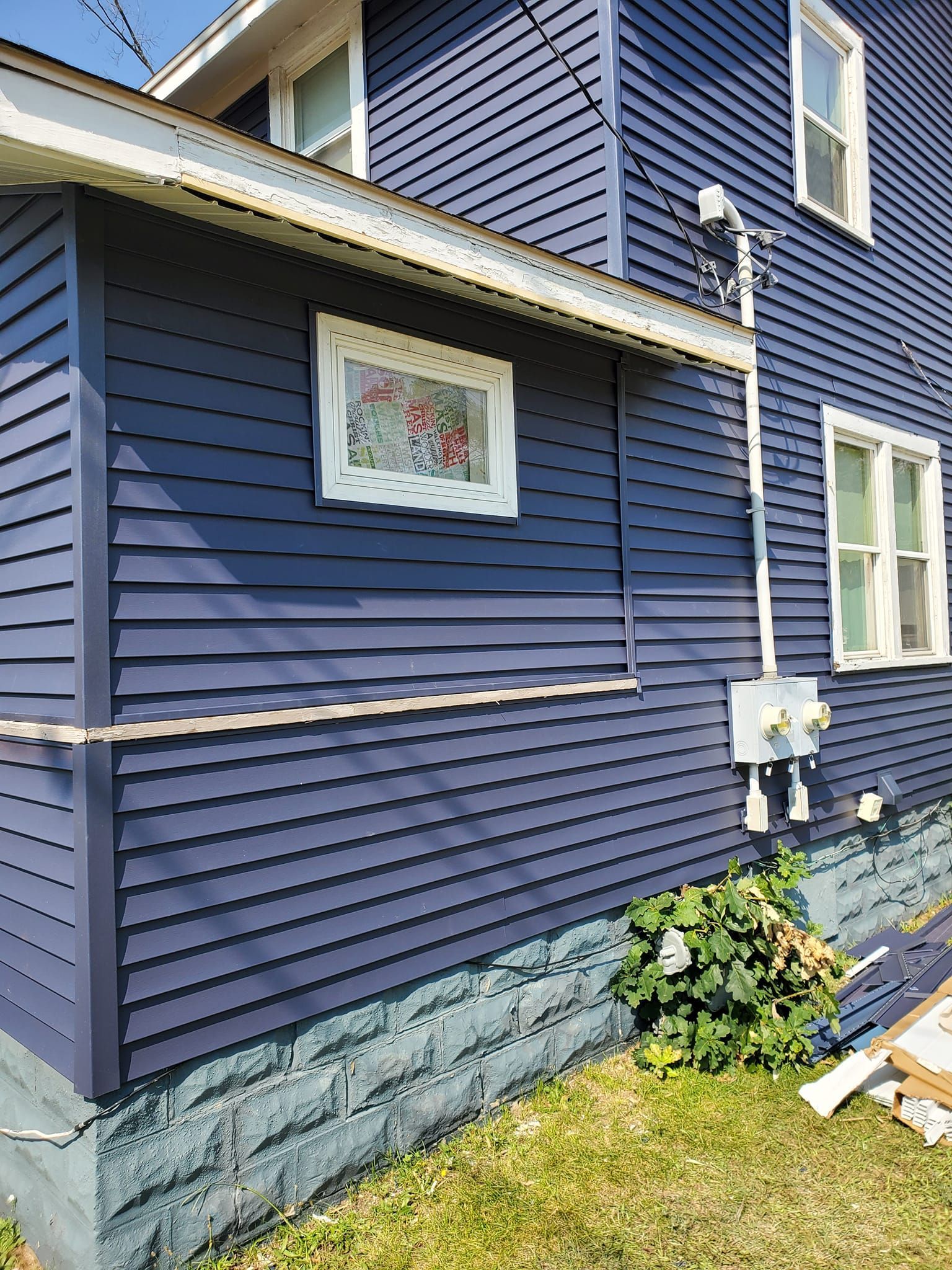 Blue house exterior with white trim, a framed picture on the wall, and flowers near the foundation.