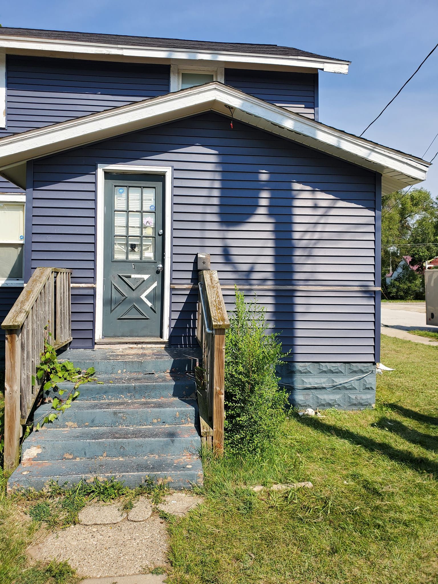 Blue house front with gray door, small porch, and concrete steps leading to a grassy yard