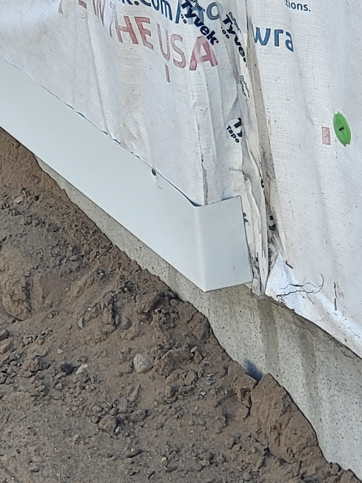 Damaged white tarp or wall covering beside muddy ground, with torn edges and exposed seam