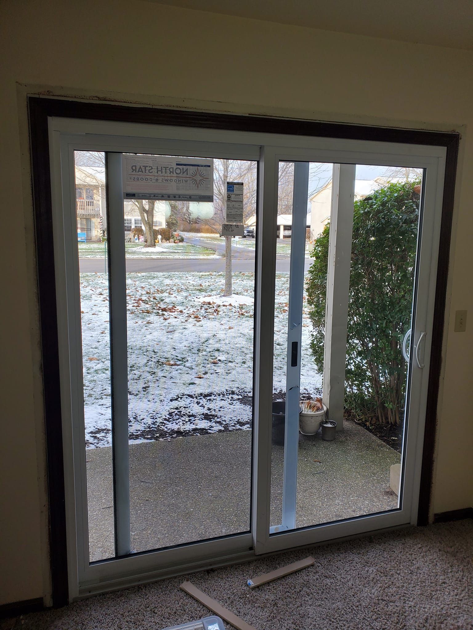 Sliding glass door opening to a snowy outdoor patio with hedges and a gravel walkway.