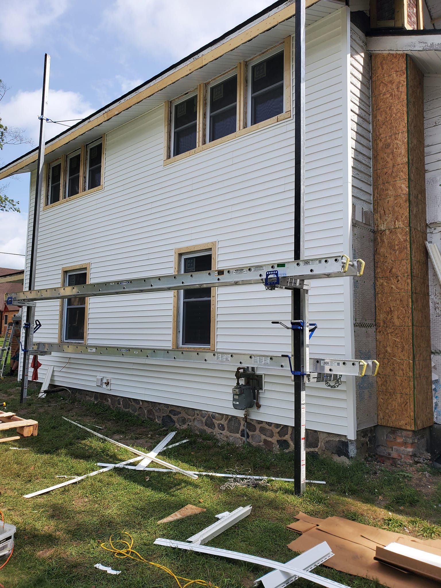 Partially renovated house exterior with scaffolding, white siding, and open window frames