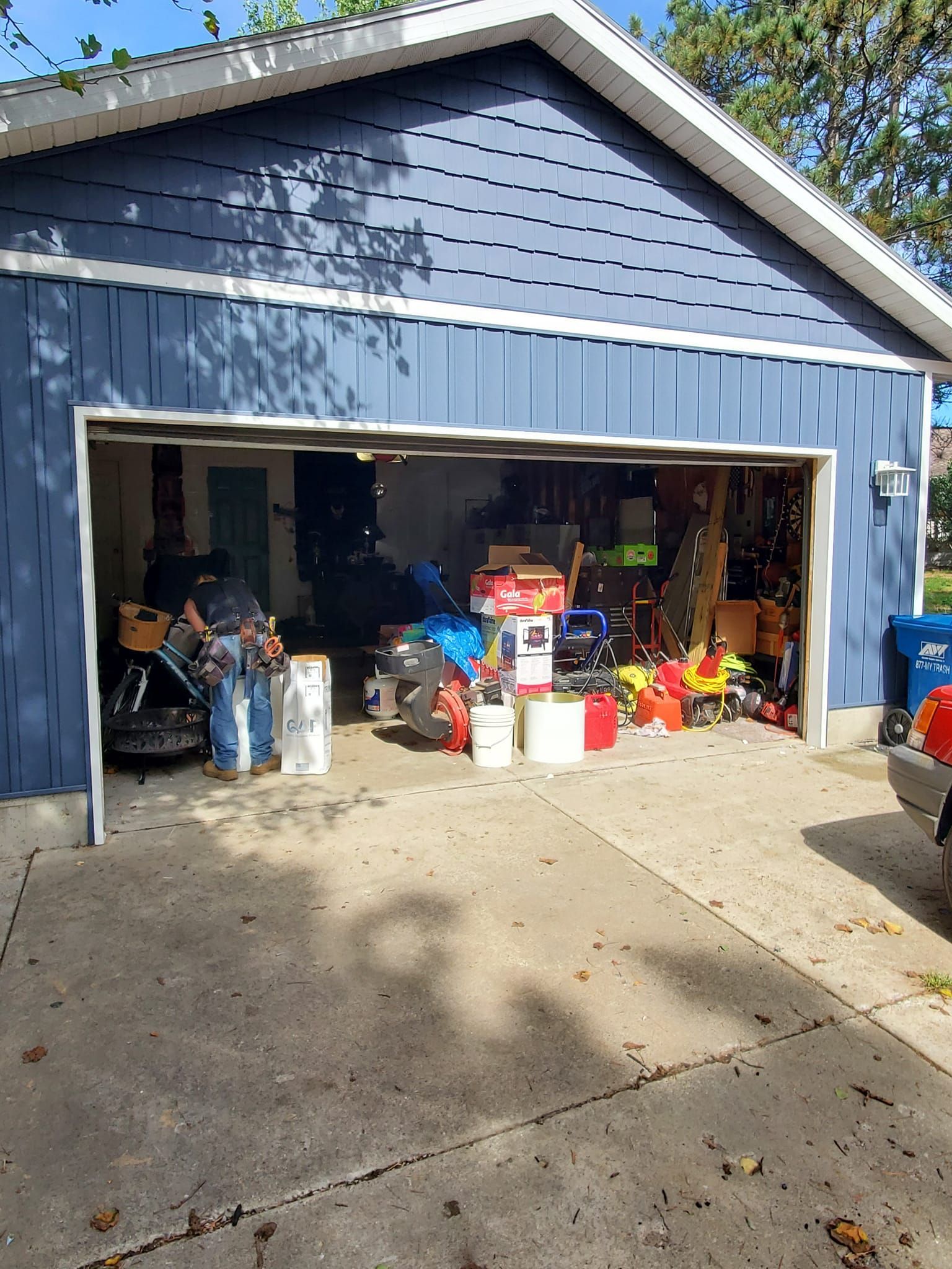Open garage filled with assorted items, bins, and tools in front of a blue house.