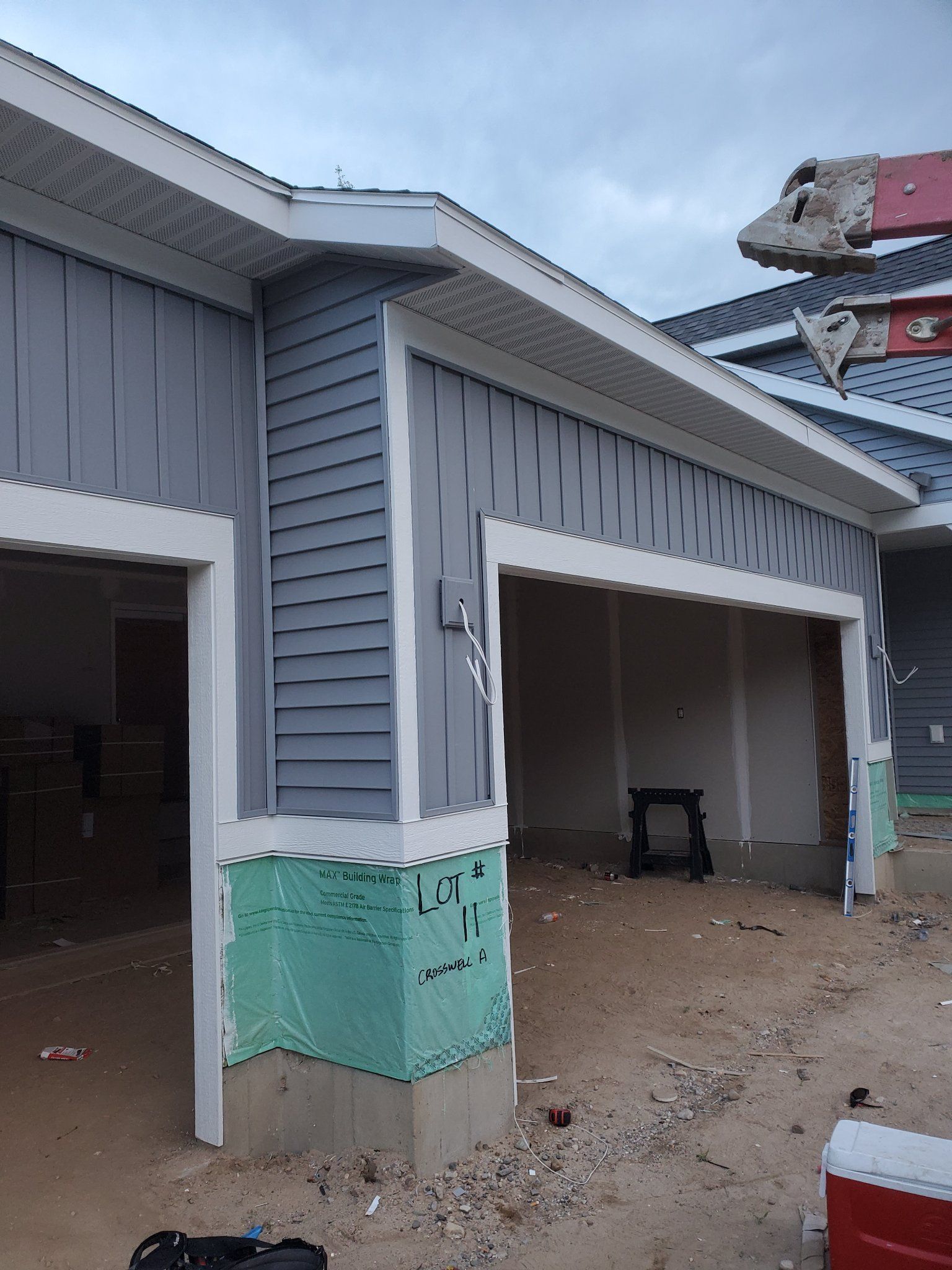 Gray house exterior with teal foundation, two open garage bays, and construction equipment nearby