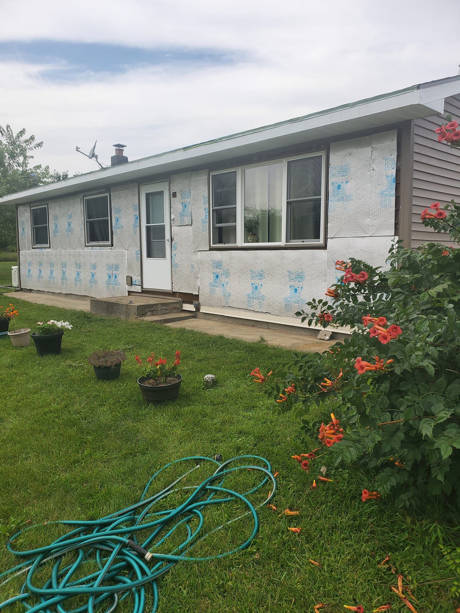 Single-story white house with blue trim, green lawn, flower pots, and a coiled garden hose in front