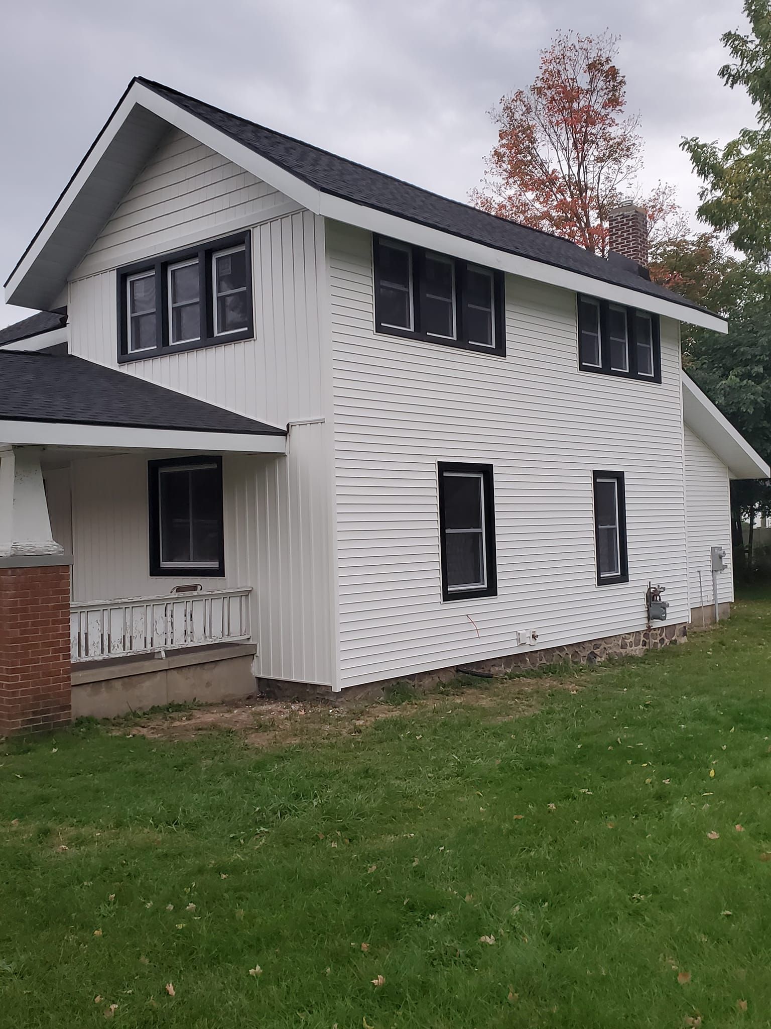 White two-story house with dark trim and a small covered porch on a grassy lawn