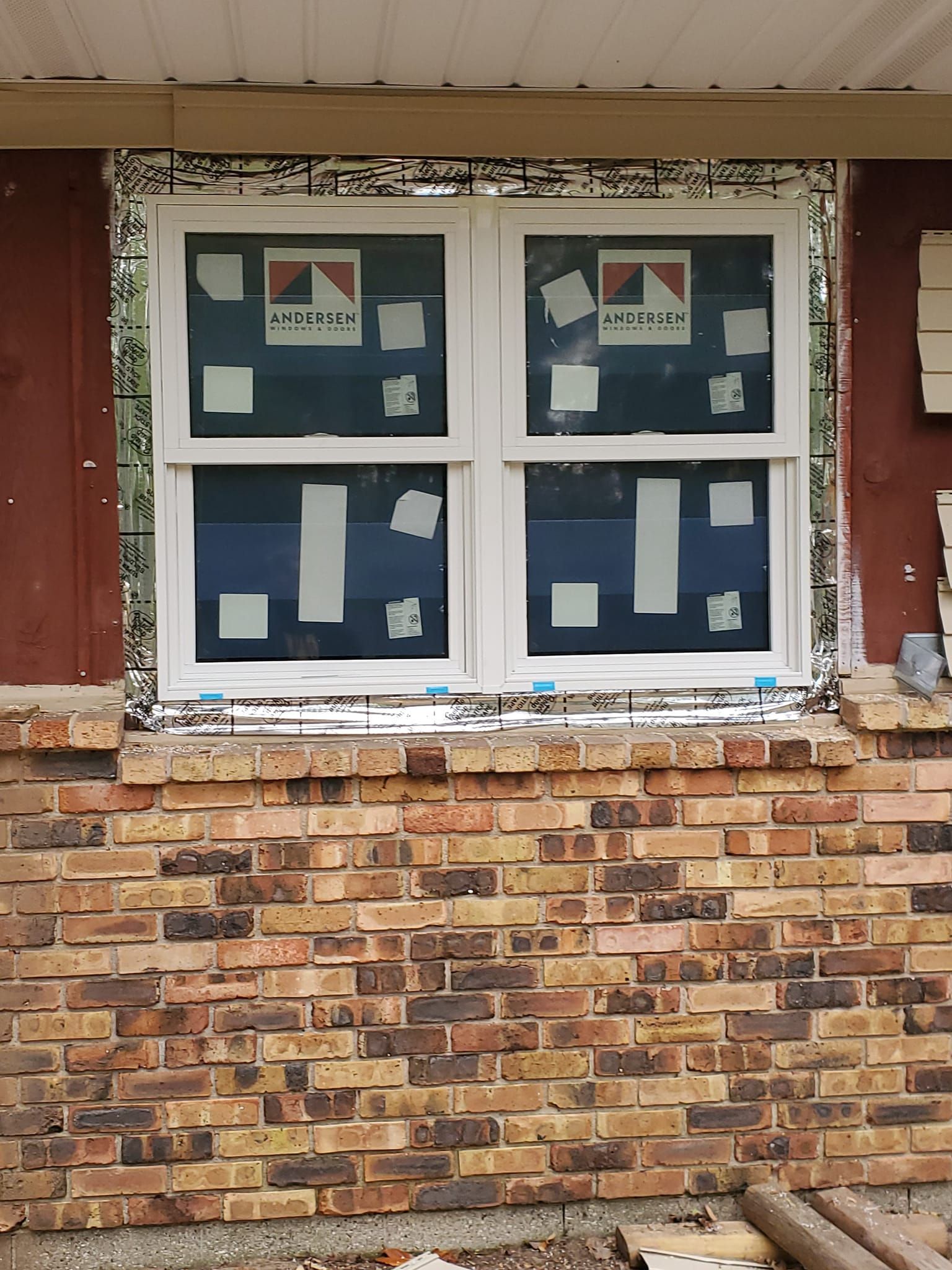 Brick wall with a white-framed window displaying four blue posters or drawings behind the glass.