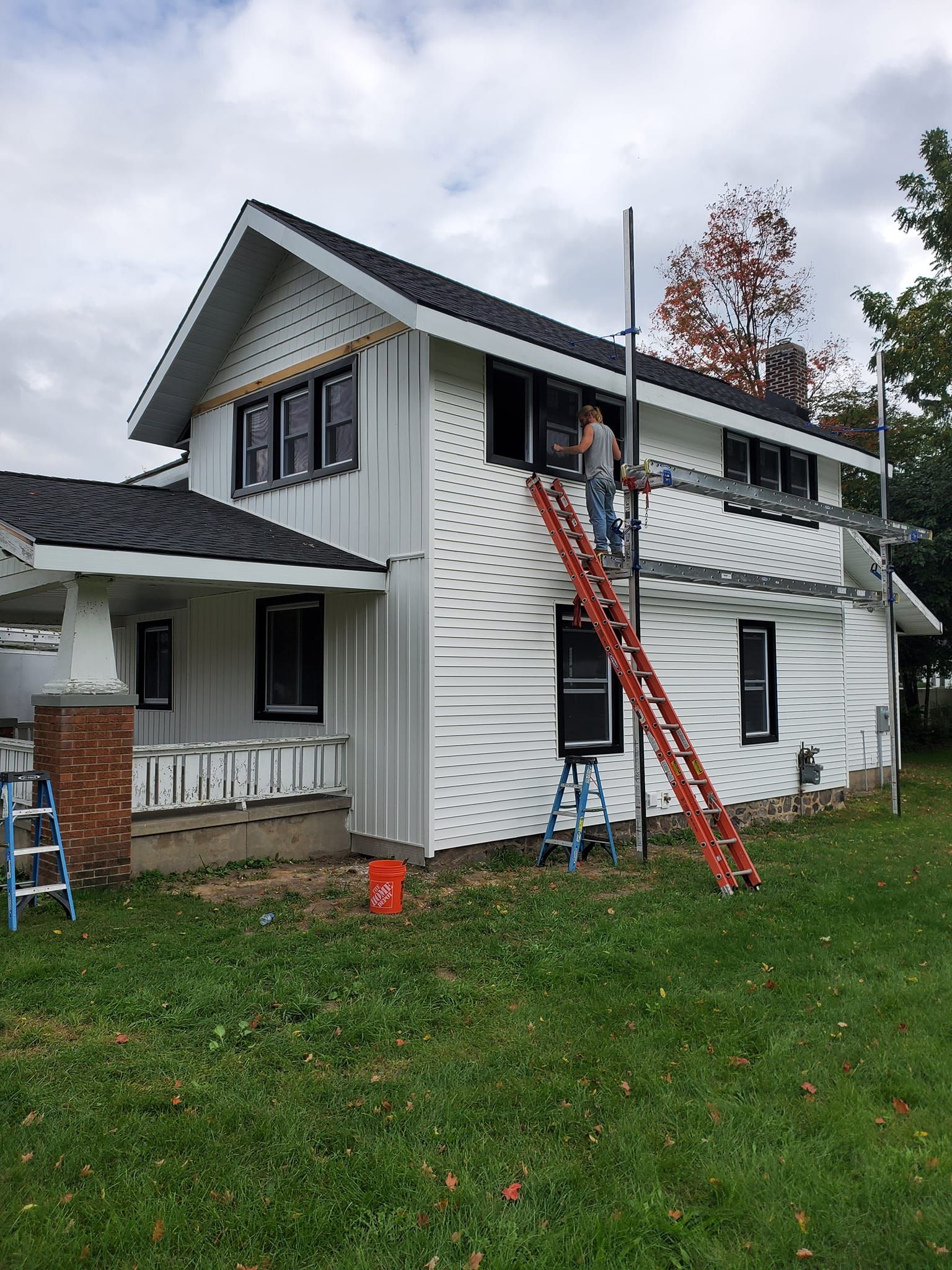 Two-story house with white siding, a red extension ladder, and workers on the roof during repairs.