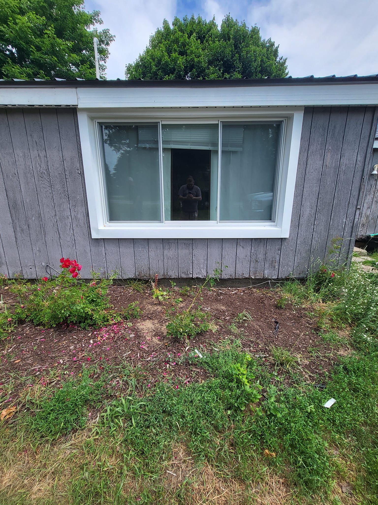 House exterior with a white window, gray siding, and a small flower bed in front