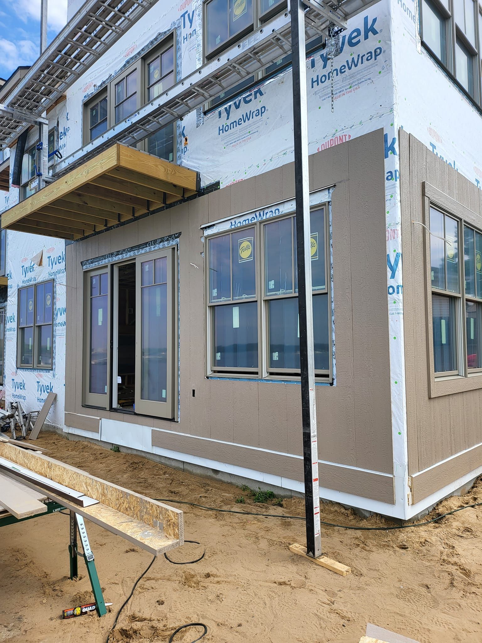 Partially built house exterior with tan siding, windows, and a small porch over bare dirt