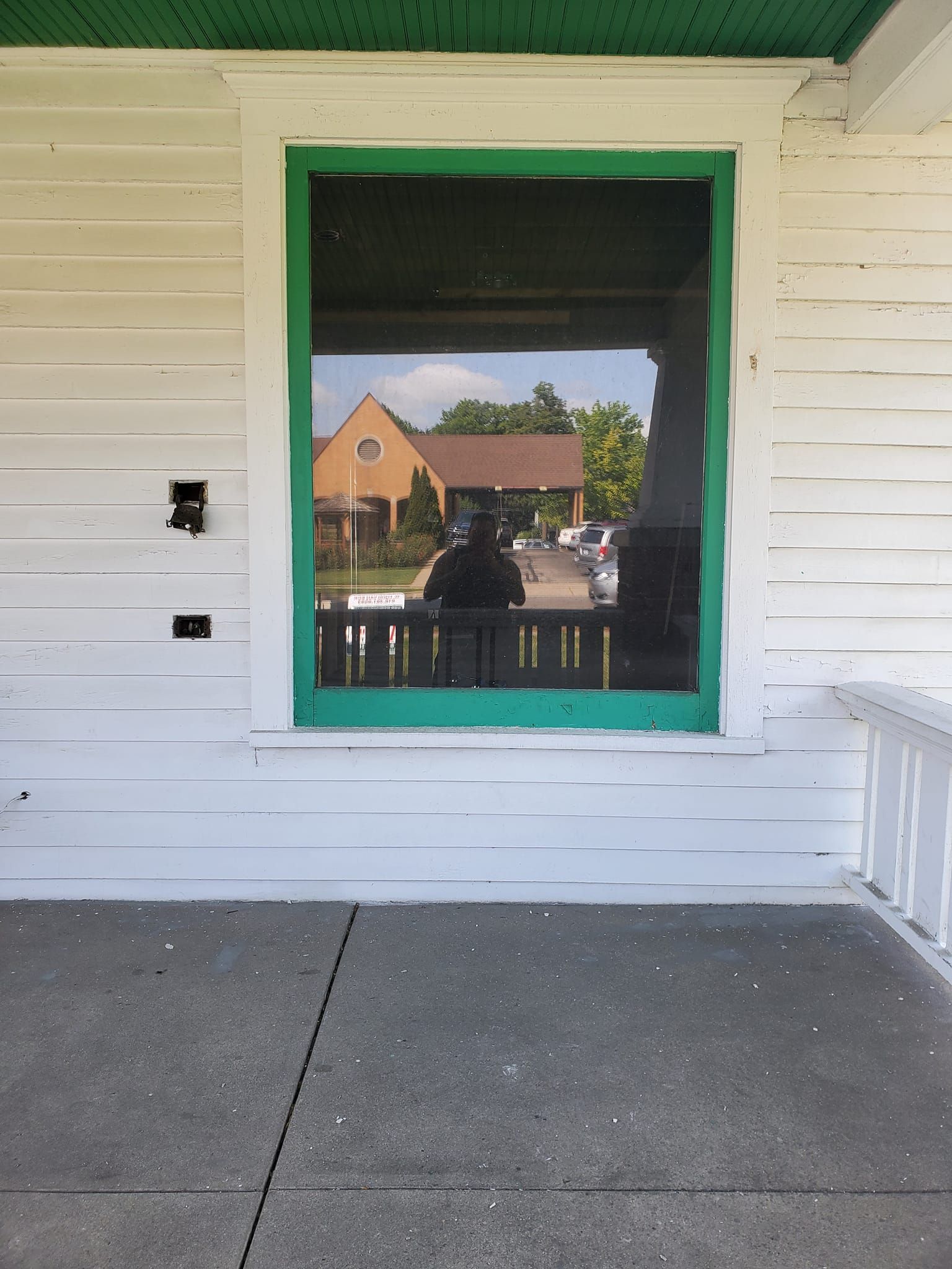 White porch wall with a green-trimmed window opening and a concrete floor, reflecting houses outside.