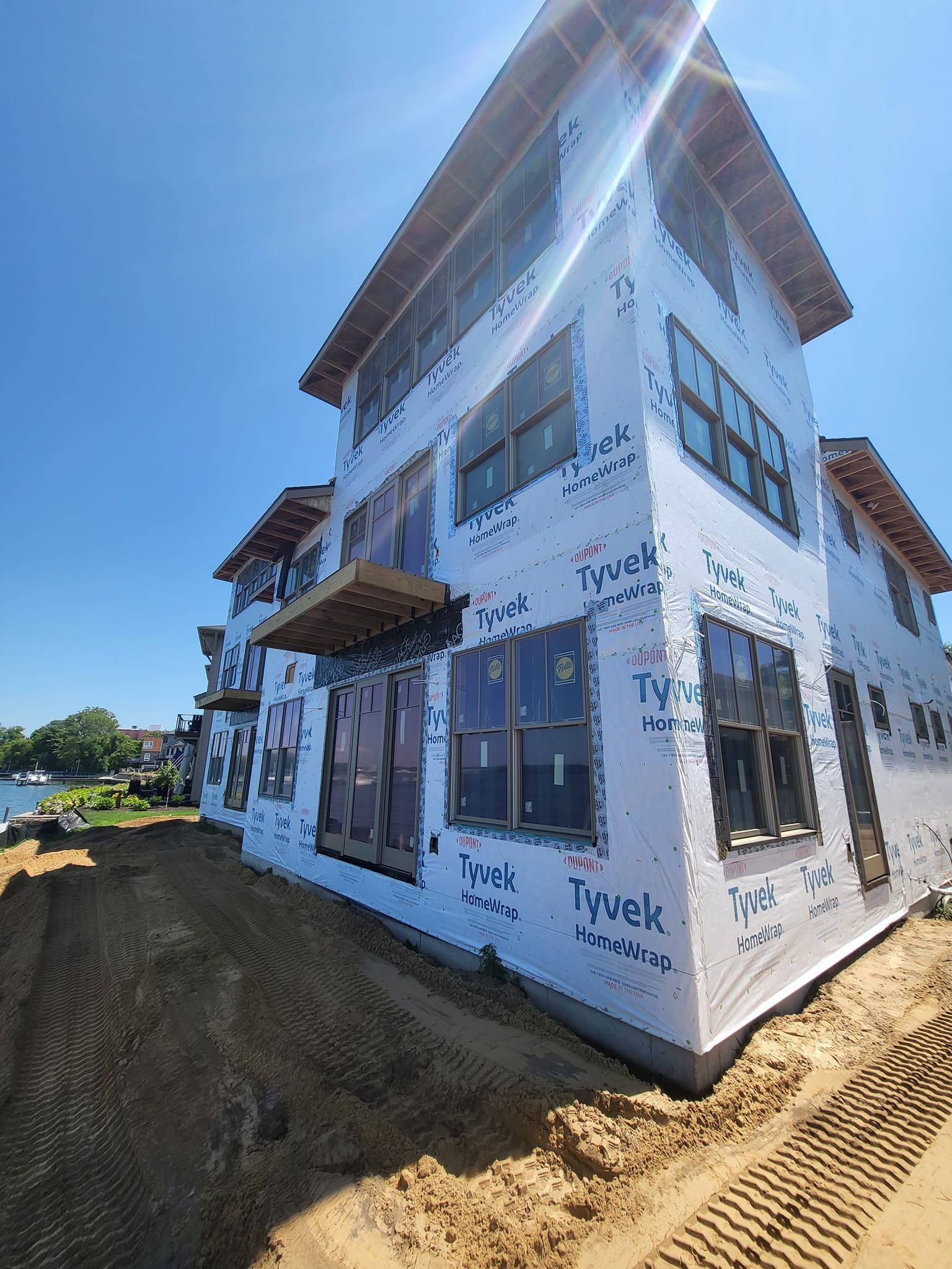 Partially built white house wrapped in Tyvek under a bright blue sky at a construction site