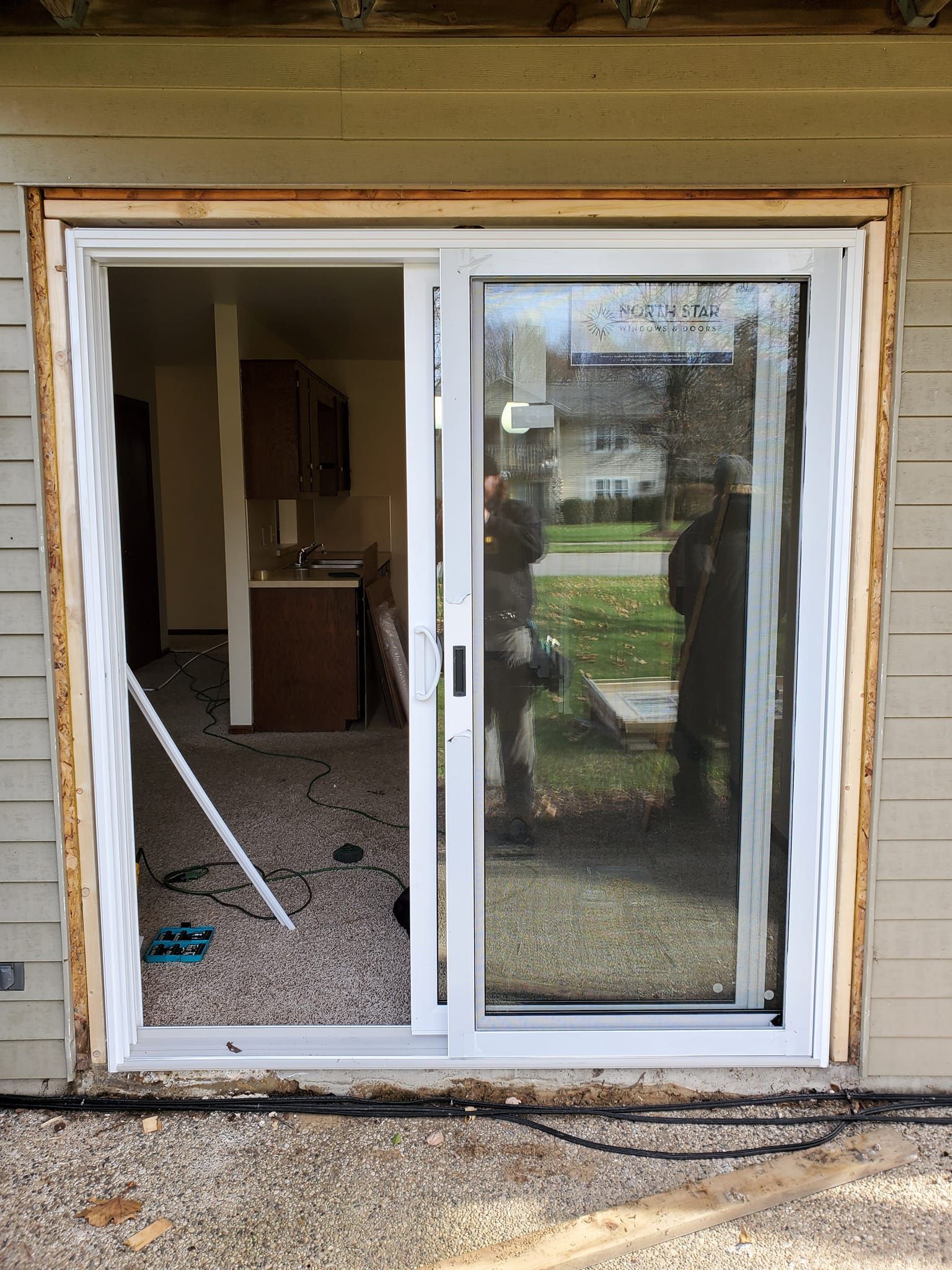 Damaged white sliding glass door leading into a home, with broken glass and debris inside