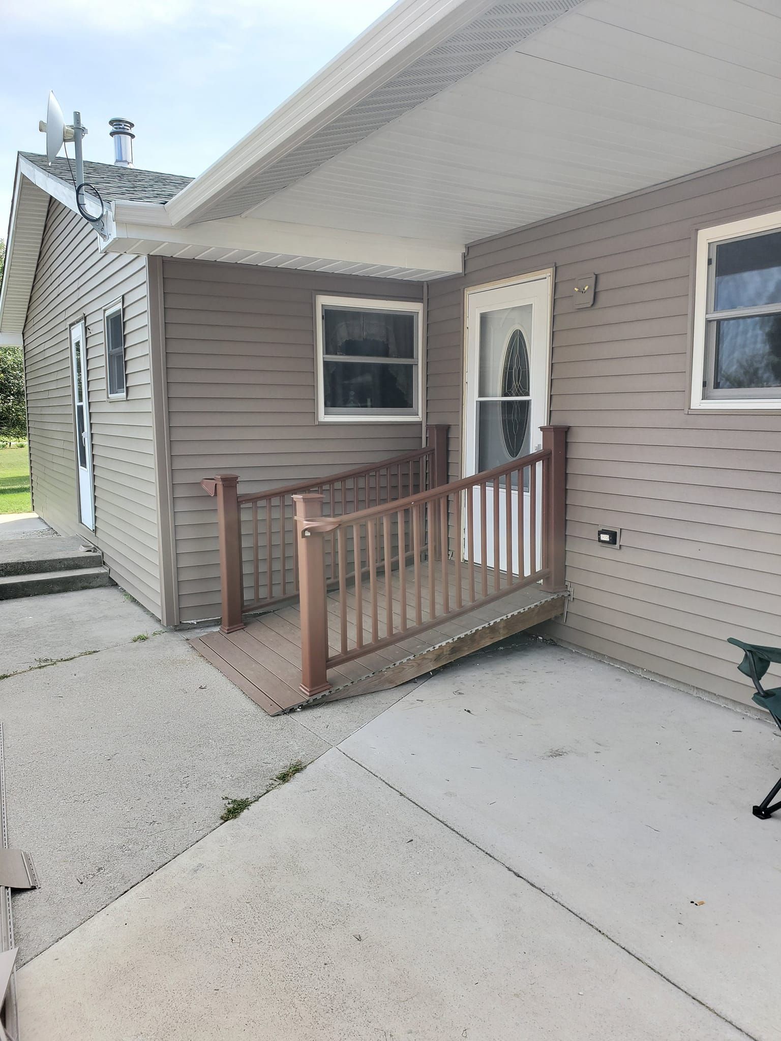 Exterior of a house entrance with a small wooden ramp, gray siding, and a concrete walkway