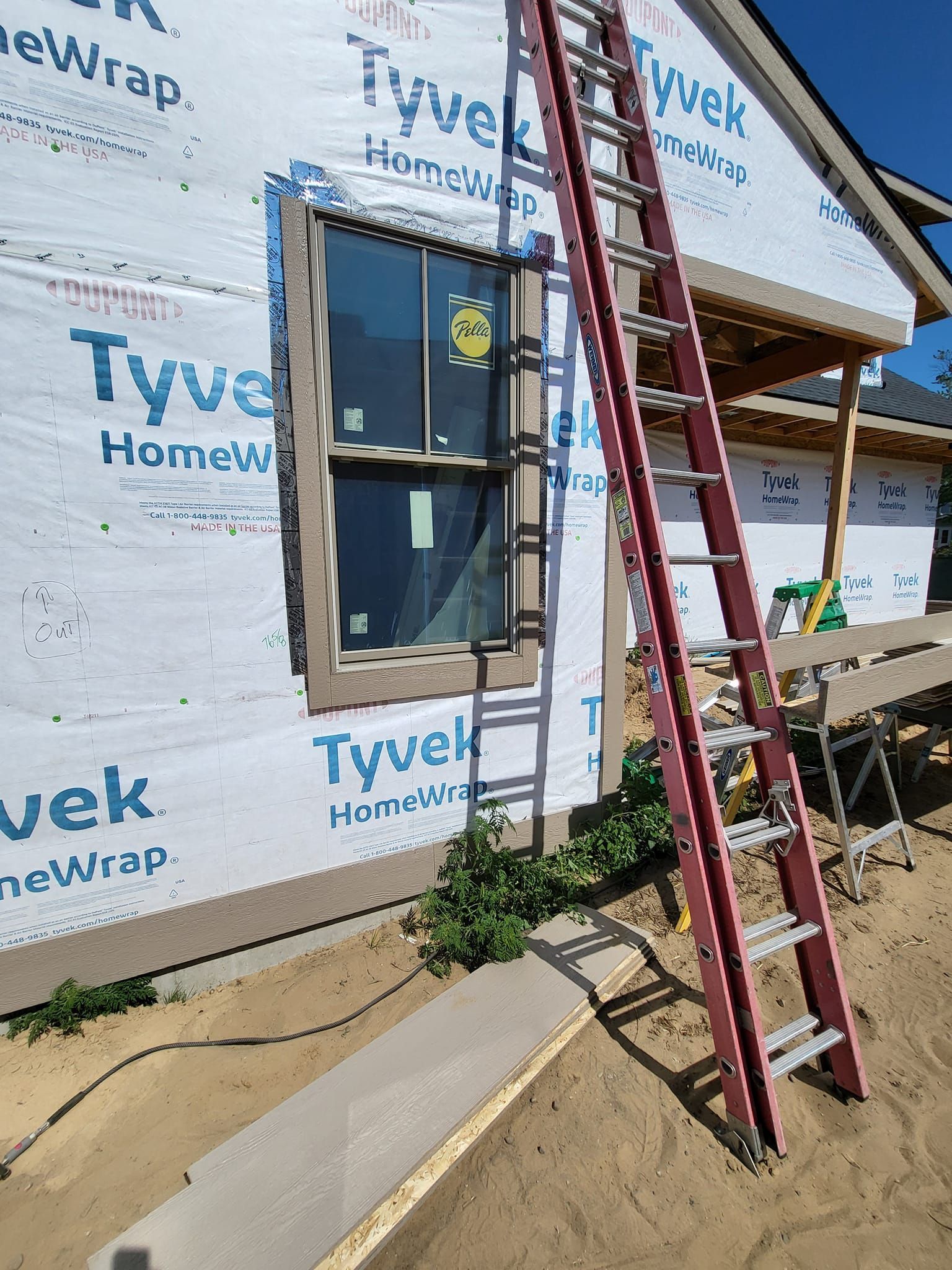 Ladder leaning against a house under construction beside a window and Tyvek-wrapped wall