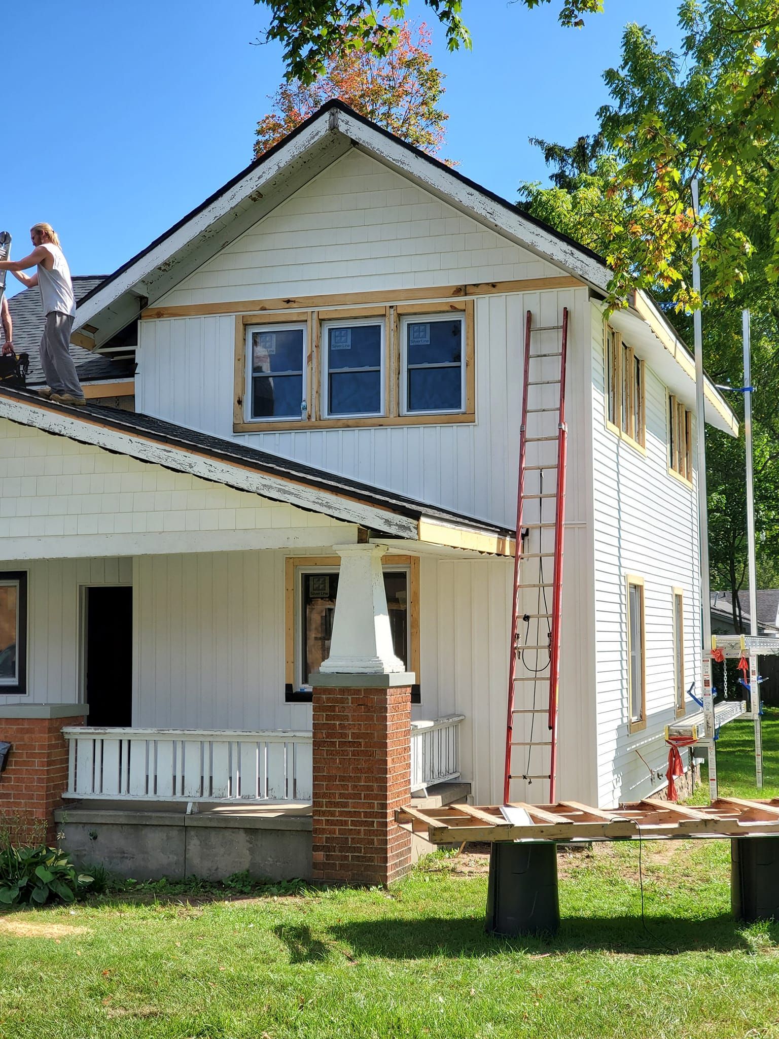 Two-story white house with a front porch, red ladder, and picnic table in a sunny yard