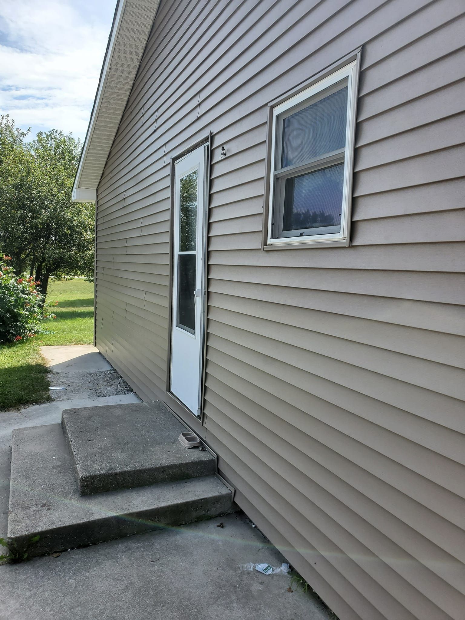 Side door of a house with concrete steps and tan siding beside a grassy yard