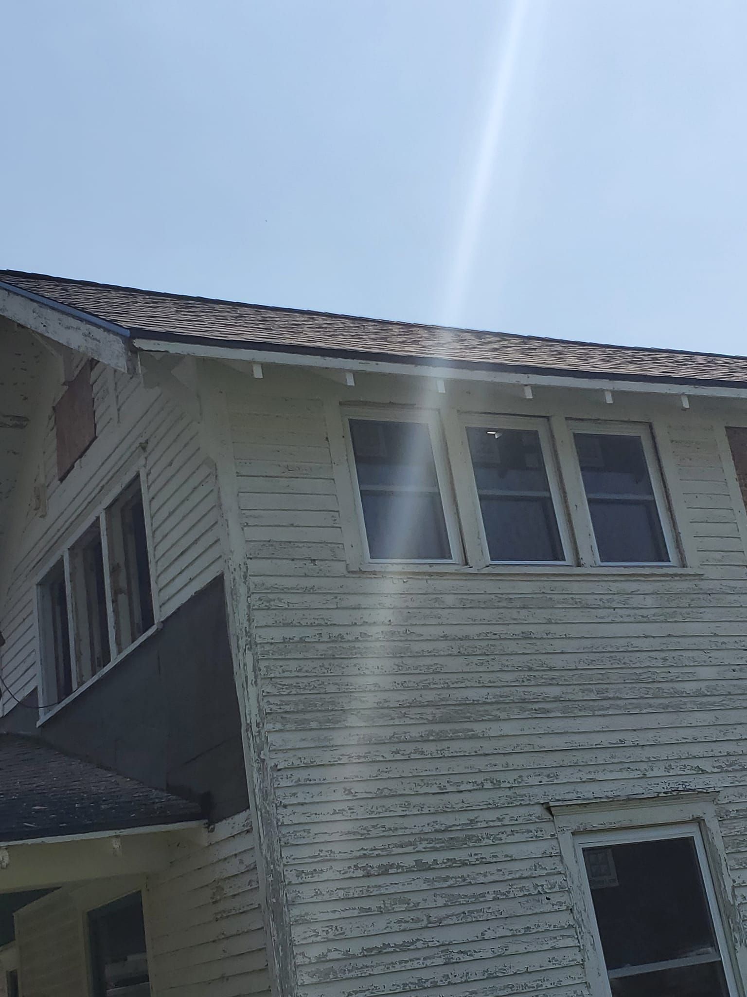 Sunlit exterior of a two-story house with white siding and a dark shingled roof