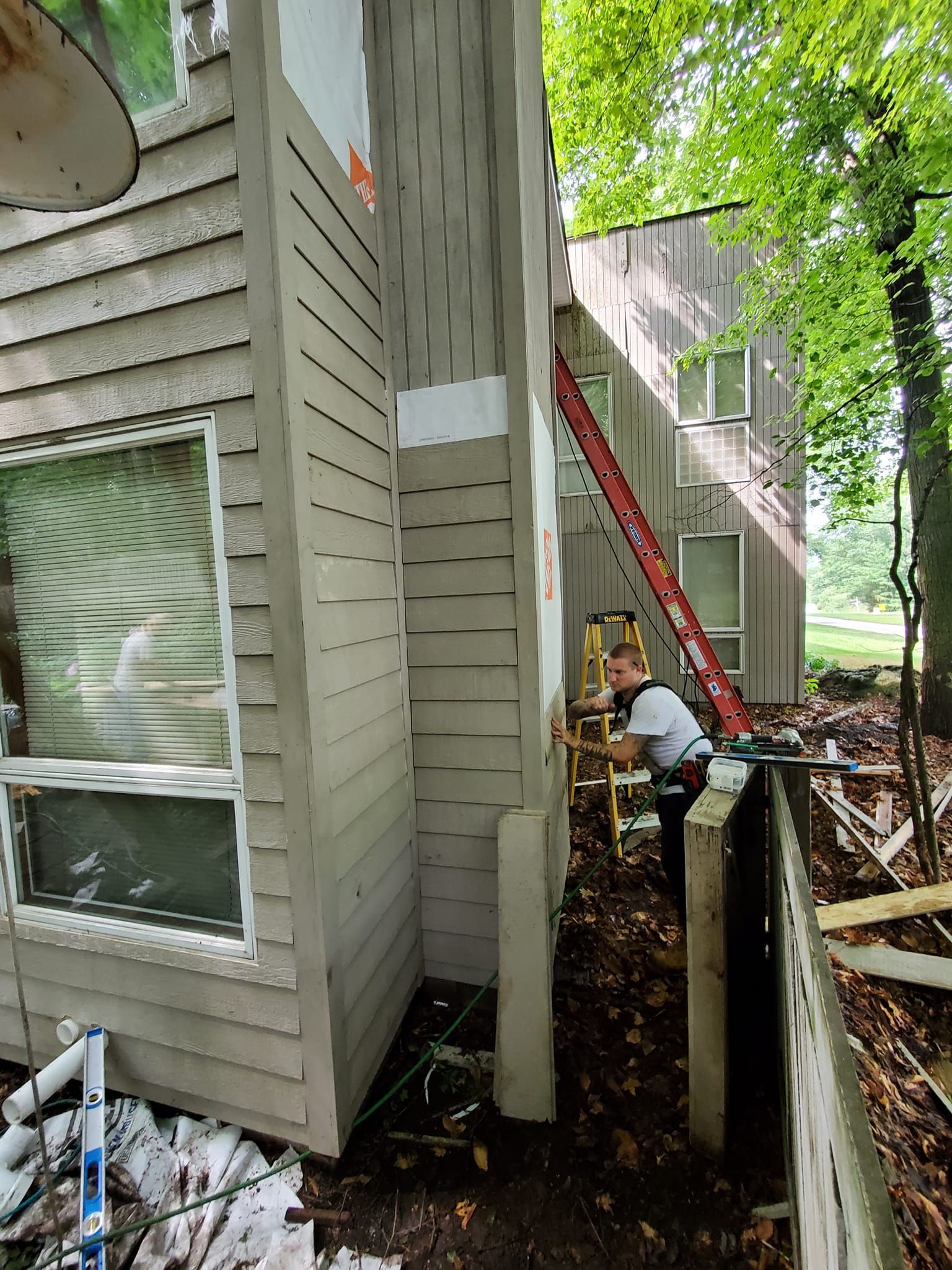 Exterior side of a house with a window, stairs, and a person crouching near the foundation fence line