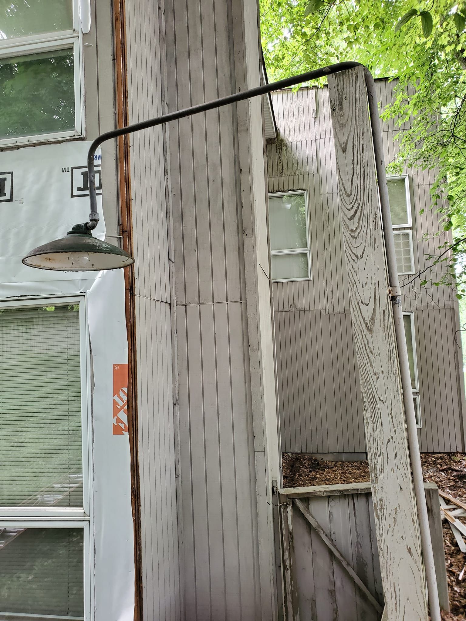 Outdoor metal spiral staircase beside a building, with black railing and gray steps amid trees.