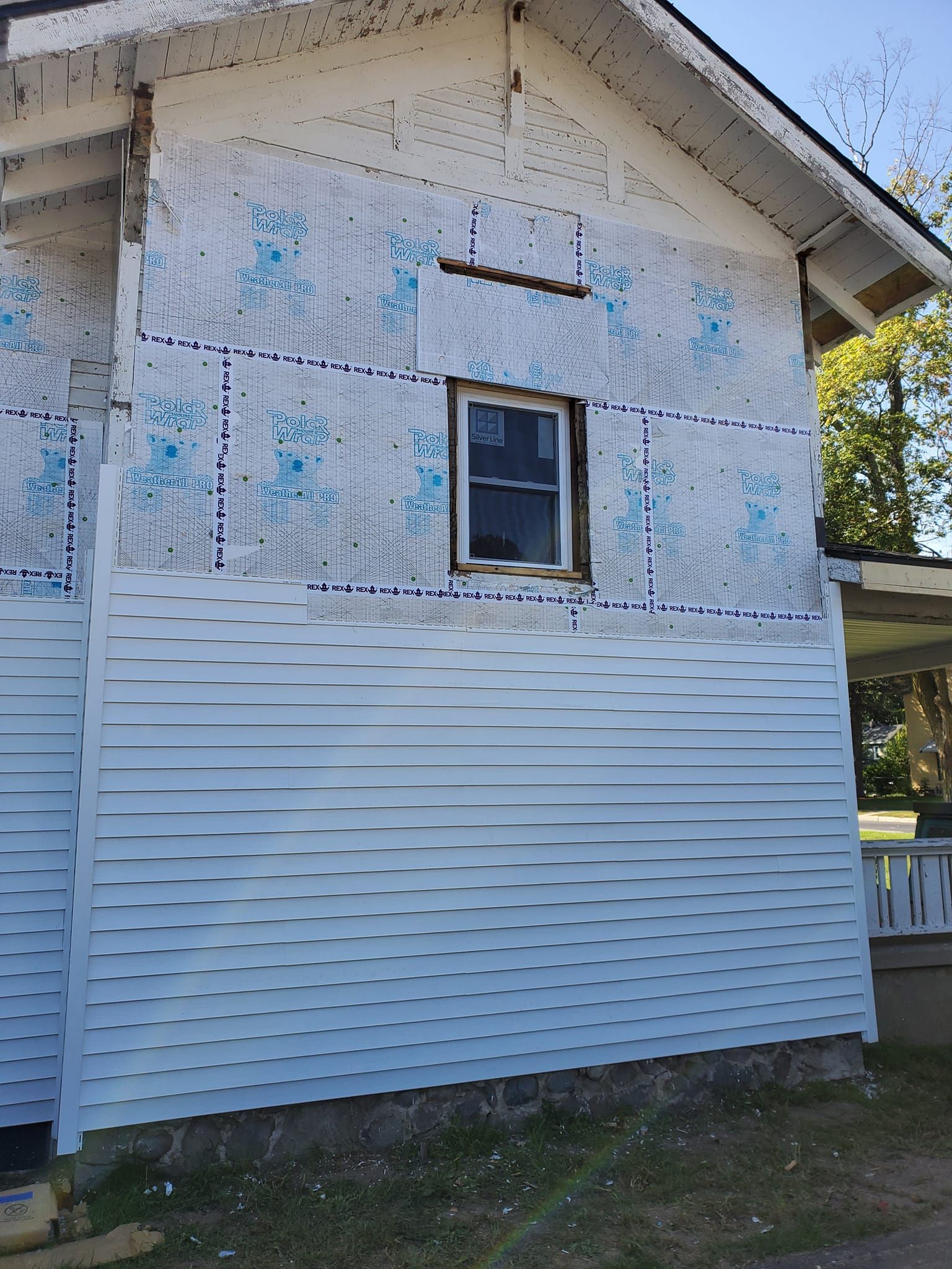 Side of a weathered house with peeling blue paint and white siding, showing a small window under the roofline.