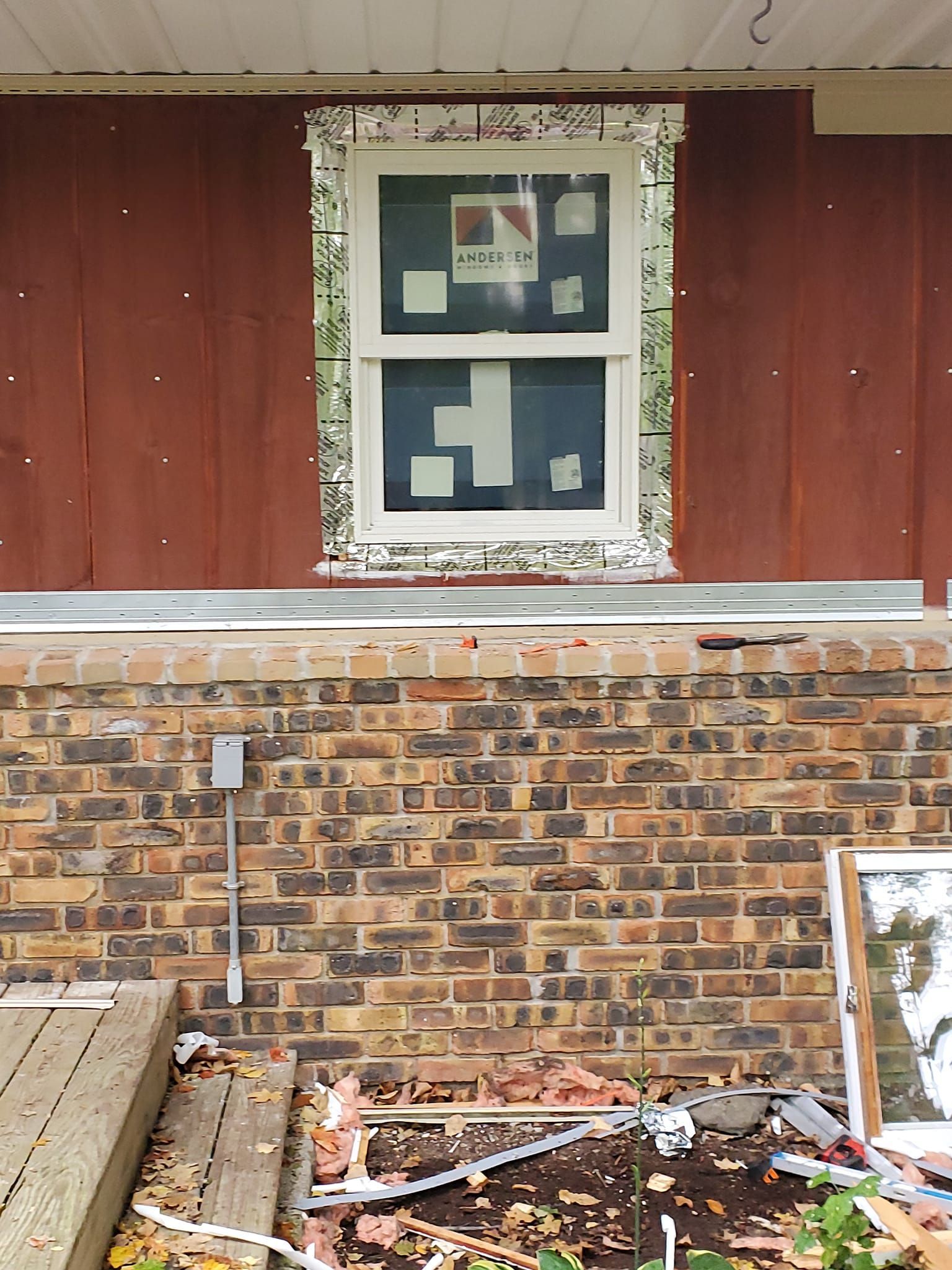 Broken window in a red and brick wall above debris and a porch railing.