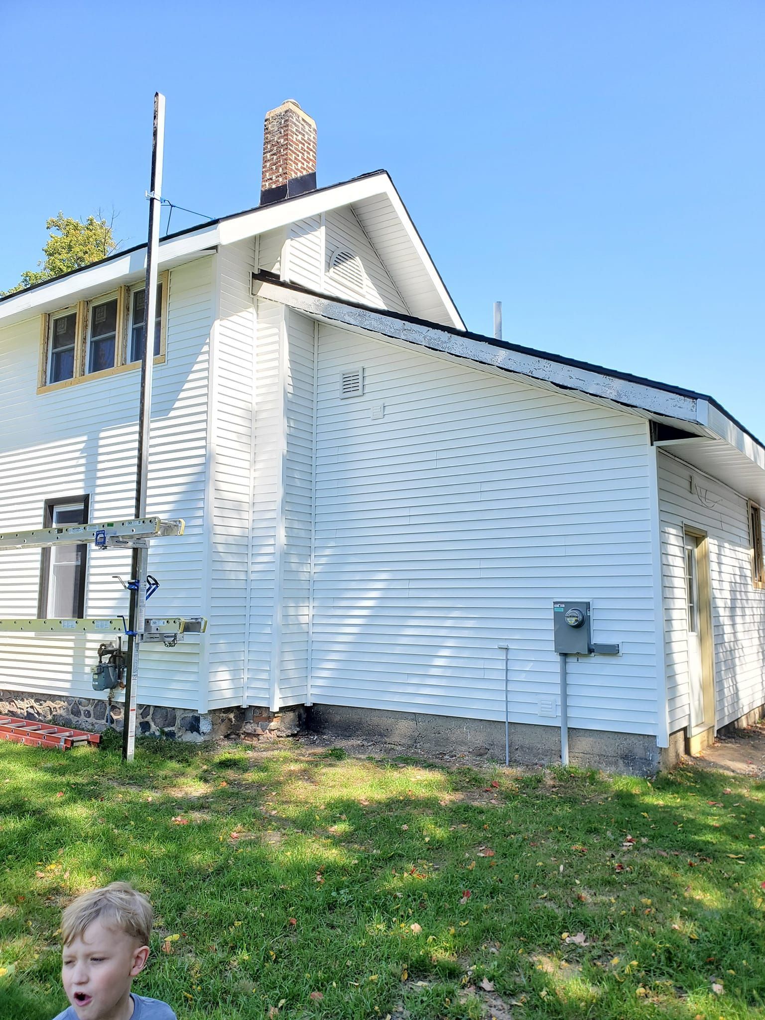 White house with vinyl siding, chimney, utility poles, and grassy yard under a clear blue sky