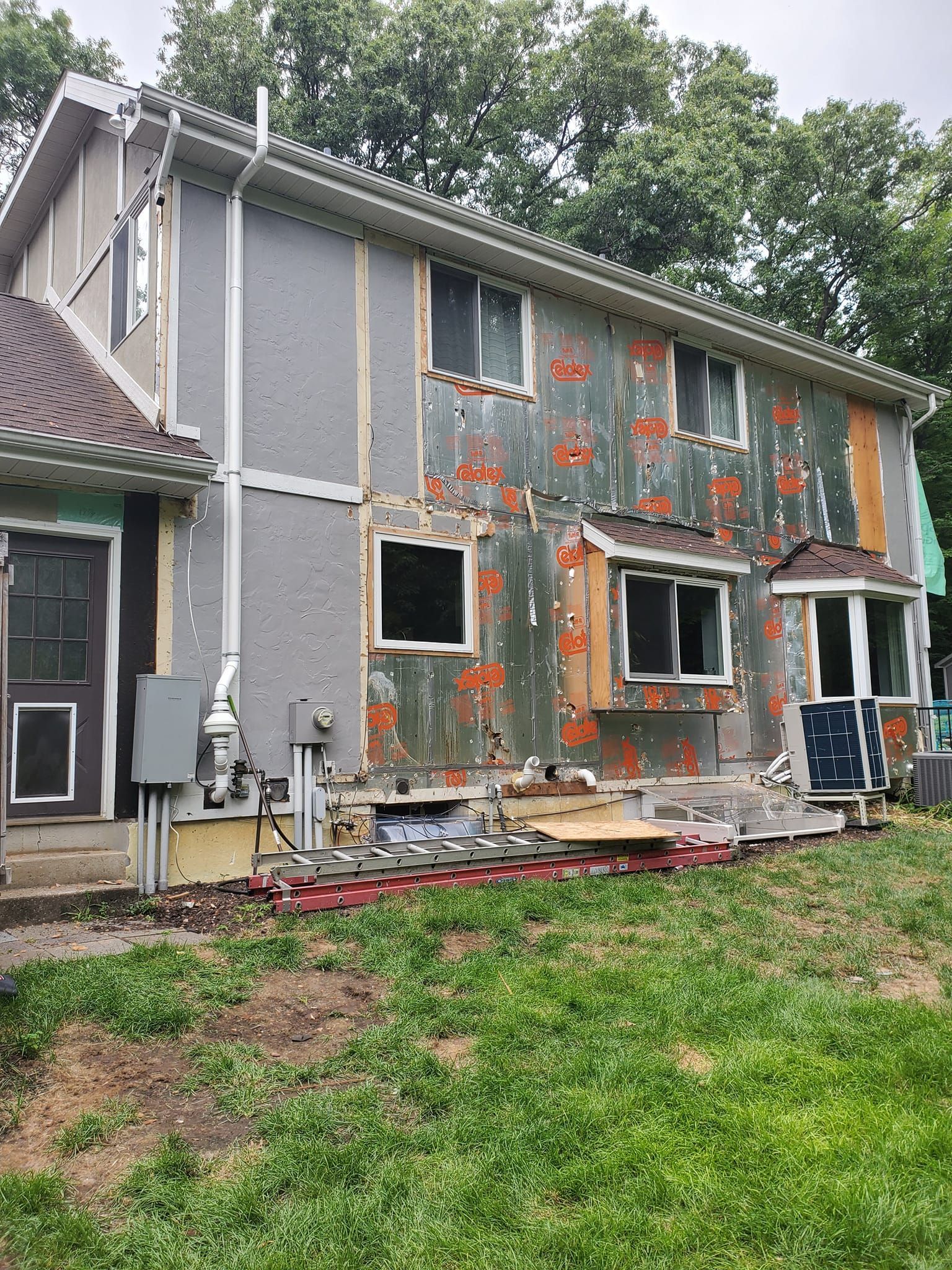 Two-story house with torn gray siding and exposed insulation, showing severe exterior damage.