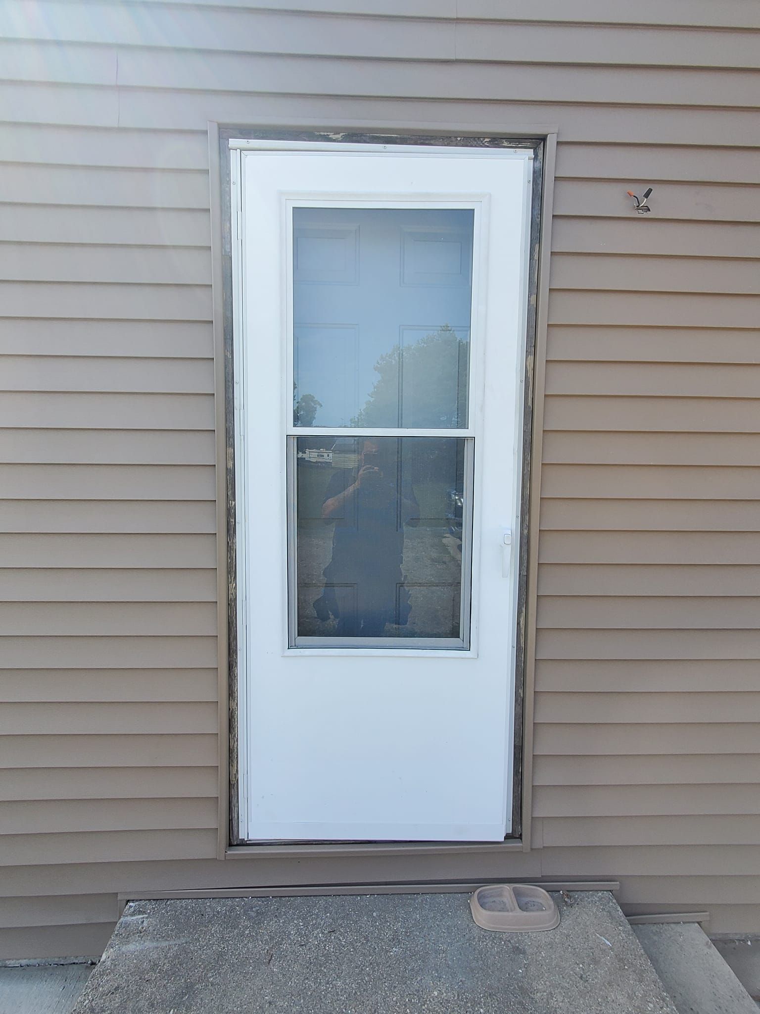 White exterior door with window in beige siding wall, next to a small concrete step.