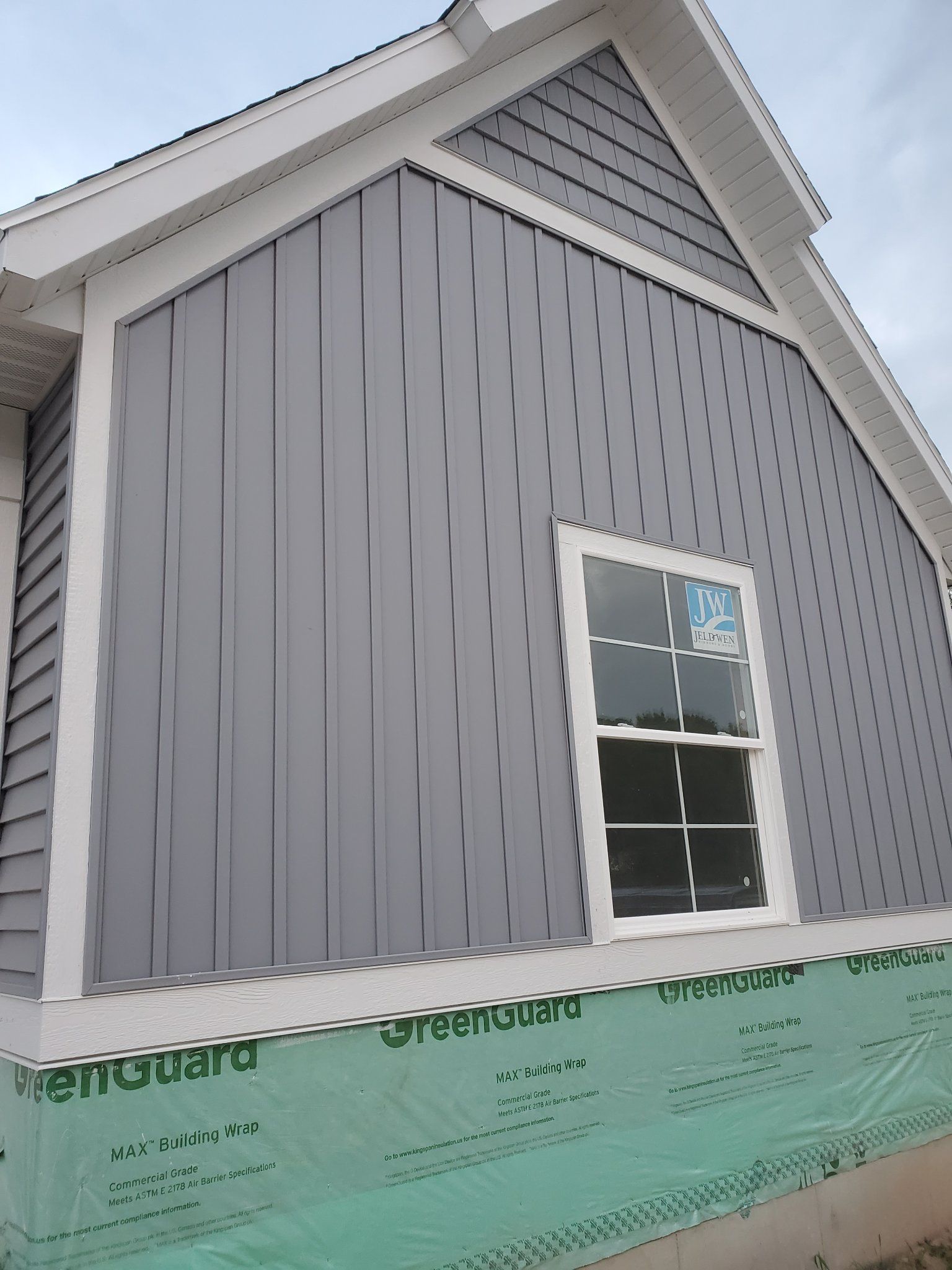 Gray house exterior with white trim and a single window above green construction wrap