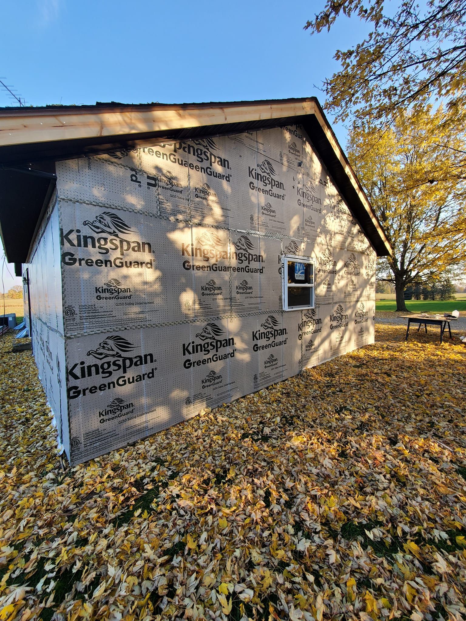 Kingsham House under construction, wrapped in branded sheeting beside a tree covered in autumn leaves.