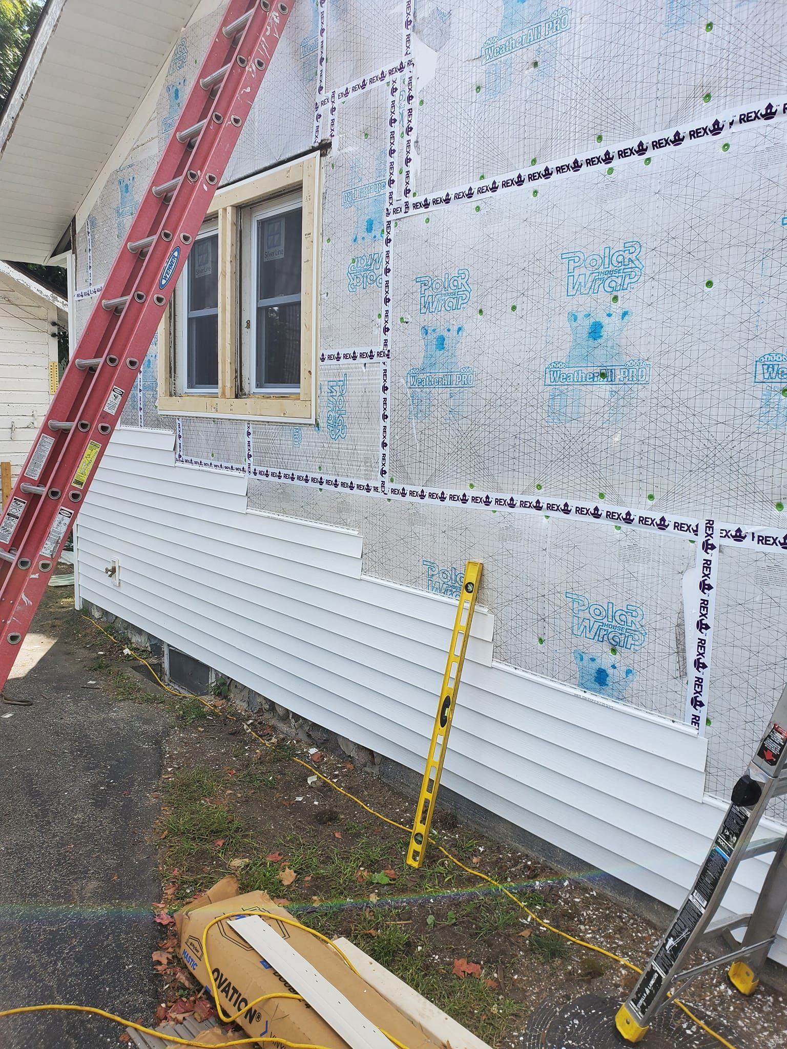 House exterior under renovation with ladder, window, and white siding panels installed along the wall