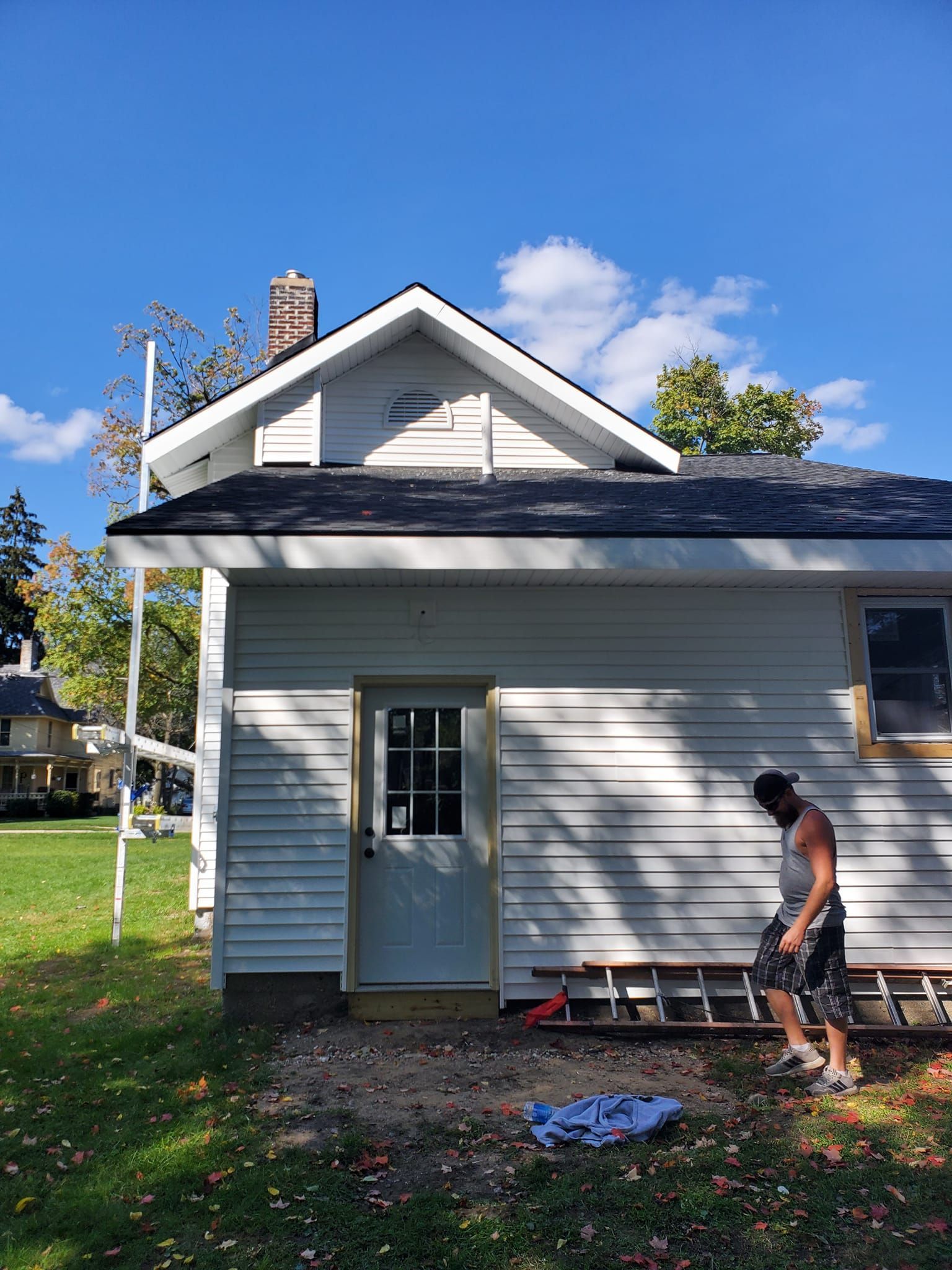 Person painting the side of a gray house with a roller on a sunny day