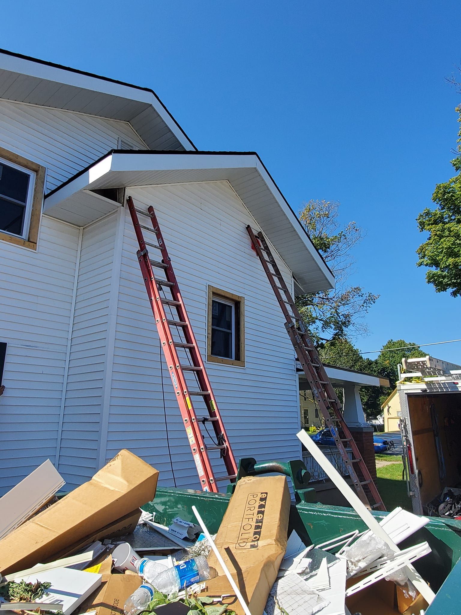 Ladder leaning against a white house with scattered debris and construction materials in the yard