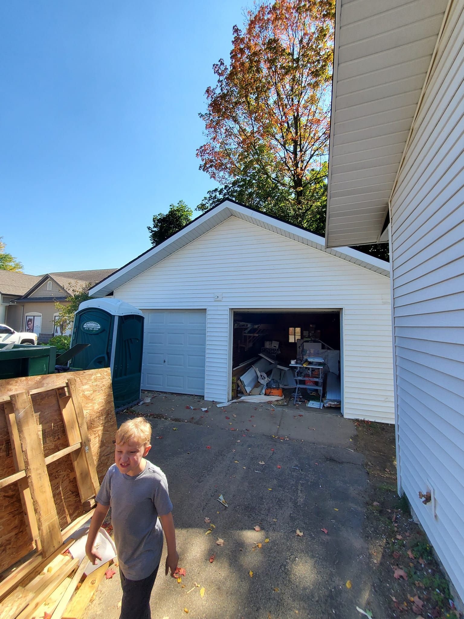 Backyard view of a white detached garage with open door and a person walking on gravel driveway